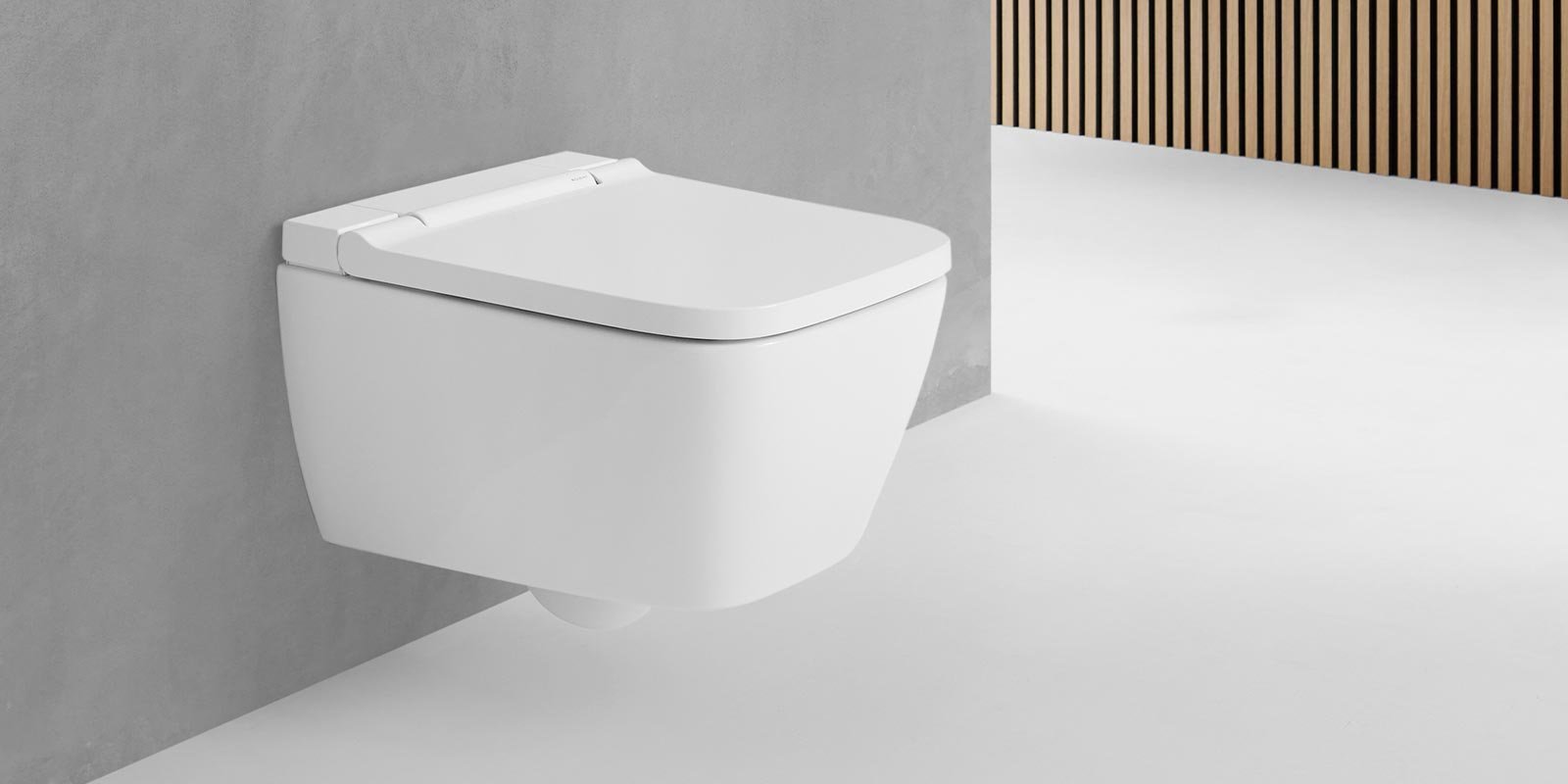 Eine moderne, wandmontierte Toilette in strahlendem Weiß, die elegant an einer grauen Wand angebracht ist.