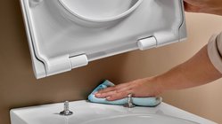  Eine Hand wischt mit einem blauen Tuch über die Oberfläche einer weißen Toilette, während der Deckel geöffnet ist. 
