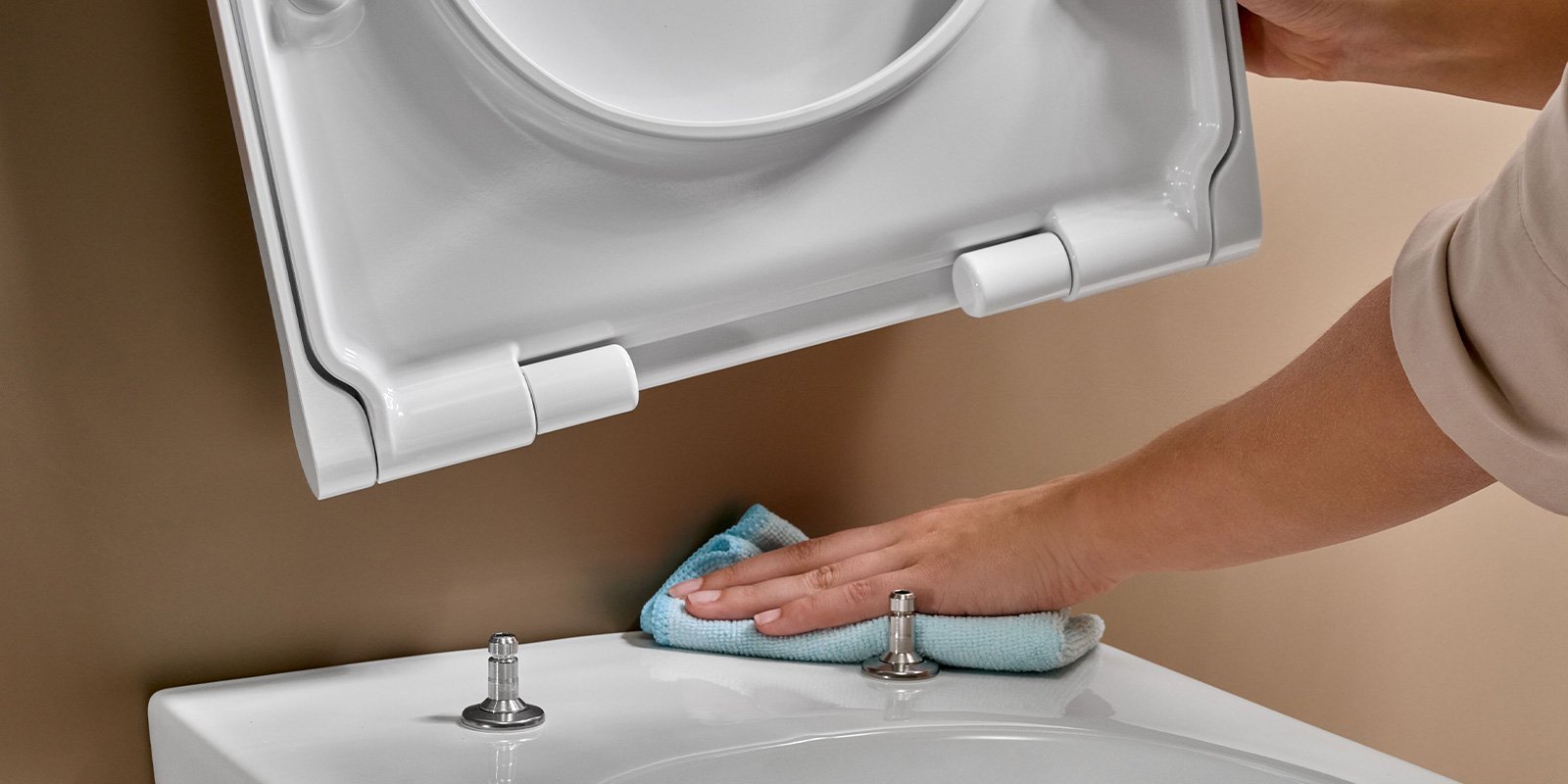  Eine Hand wischt mit einem blauen Tuch über die Oberfläche einer weißen Toilette, während der Deckel geöffnet ist. 