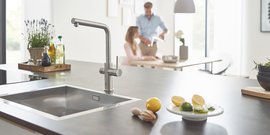 Eine moderne Küche mit einem eleganten Wasserhahn, frischen Zutaten und einem Paar, das am Tisch interagiert.